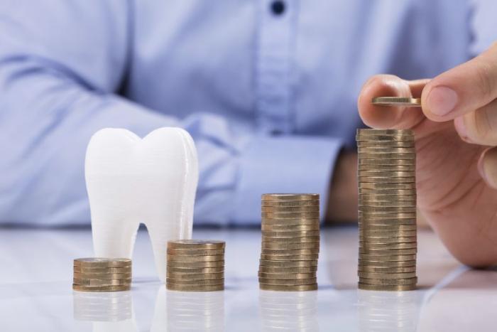 A concept image representing dental finance, featuring a white tooth model next to stacks of coins increasing in height, symbolizing the cost and savings associated with dental treatments and financial planning for dental care.